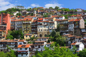 In this photo the multitude of buildings, alongside trees and vegetation, is going up the hill towards a partially cloudy sky, in Veliko Tarnovo, Bulgaria.